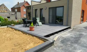 Terrasse en dalles grises sur plots, avec table et chaises, à côté d'un jardin en terre.