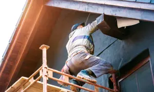 Un ouvrier en pose isolation extérieur sur un chantier, travaillant sur un bardage en bois.