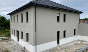 Maison neuve avec enduit de façade gris clair et soubassement blanc. Le chantier est en cours, montrant comment faire un enduit de façade.