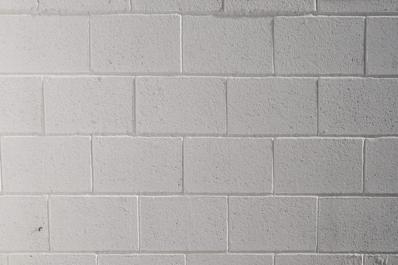 Mur de parpaings blancs, fraîchement peints au pistolet. La texture rugueuse des blocs est visible sous la couche de peinture uniforme.