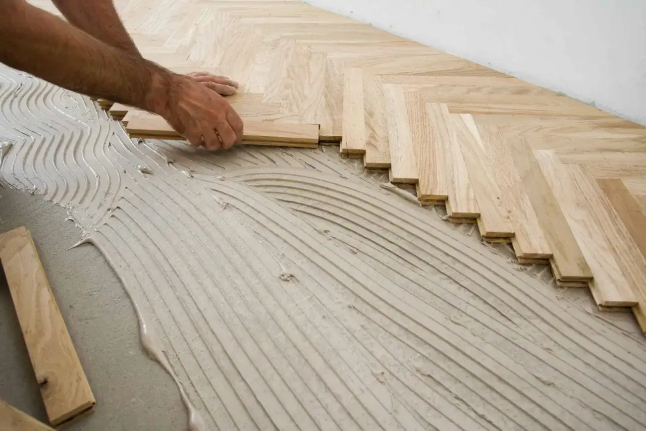 Pose de parquet en chevrons avec de la colle. L'espace entre mur et parquet stratifié est visible.