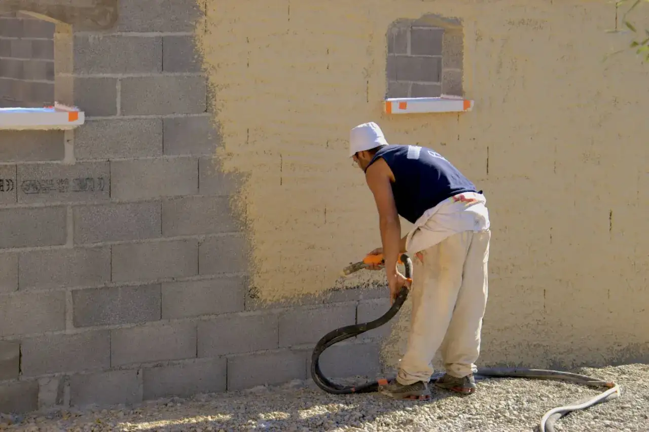 Un ouvrier utilise un pistolet pour peindre un mur en parpaings. Le crépi est appliqué en couches texturées.
