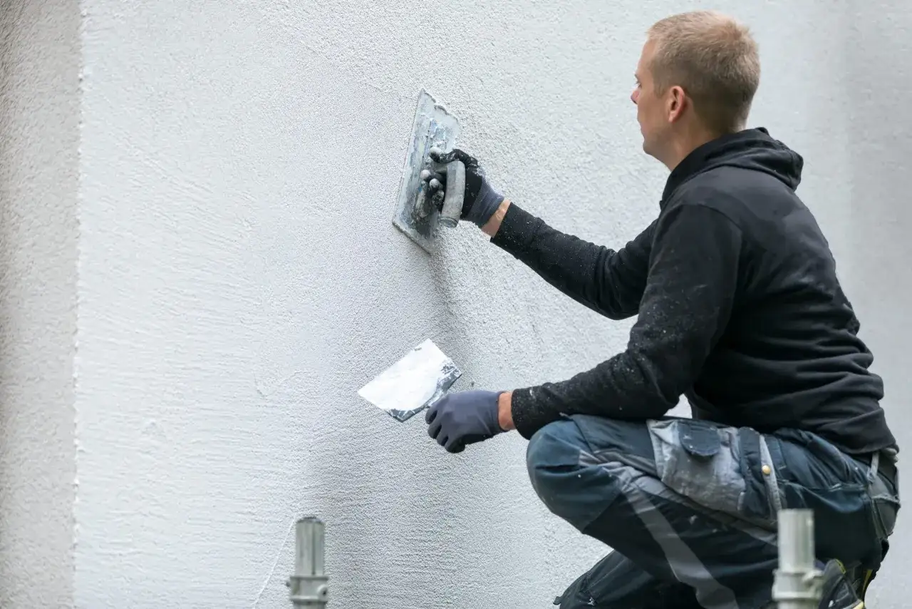 Un ouvrier applique un enduit de façade avec une truelle. Il montre comment faire un enduit de façade pour un résultat lisse et uniforme.