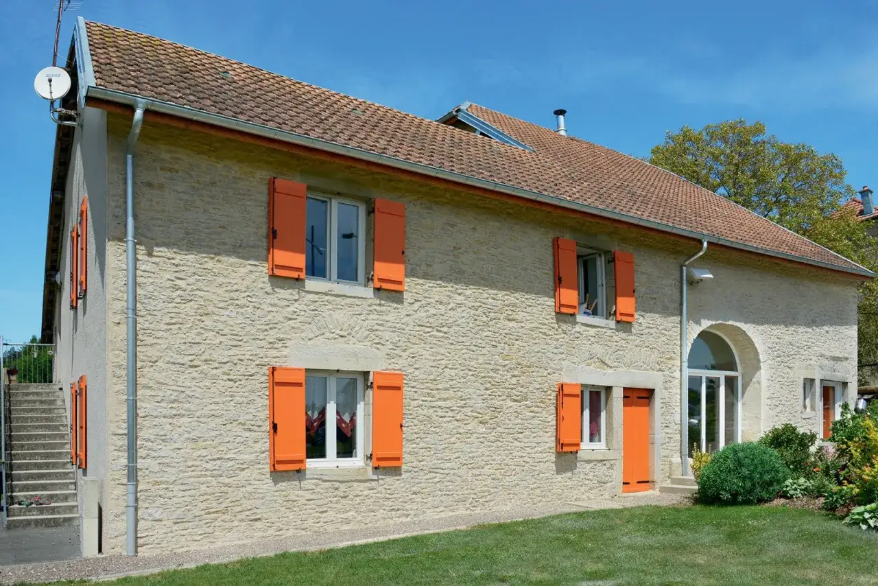 Maison en pierre avec volets en bois de couleur vive, apportant une touche joyeuse à la façade.