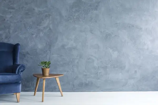 Fauteuil bleu profond devant un mur texturé en **stucco mur**. Une petite plante verte repose sur une table d'appoint en bois.
