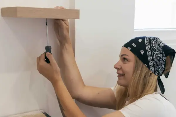 Une femme souriante utilise un tournevis pour fixer deux meubles entre eux sans percer.