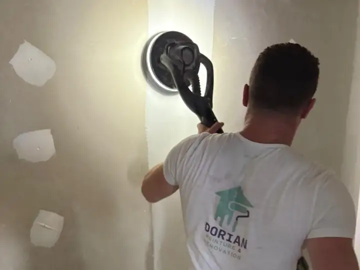 Un artisan utilise une ponceuse girafe pour lisser un mur en placo. C'est la ponceuse idéale pour un travail de finition impeccable.